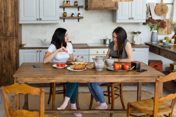 İki kız masada kek ve şekerle çay içiyor..