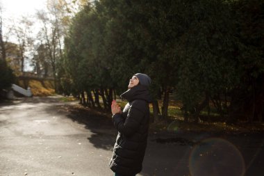 Güneşli bir günde, sıcak kıyafetler ve şapkayla parkta bir kız..