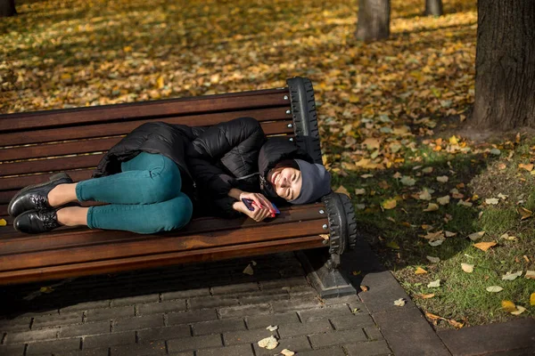 Kalın elbiseli genç bir kız parkta yatıyor ve gülümsüyor.