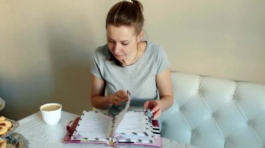 Mutfaktaki kız masadaki kanepede oturuyor, defterine yapraklar döküyor.