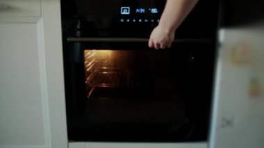 Kadınların elleri fırını açar ve turta tepsisini içine sokar..