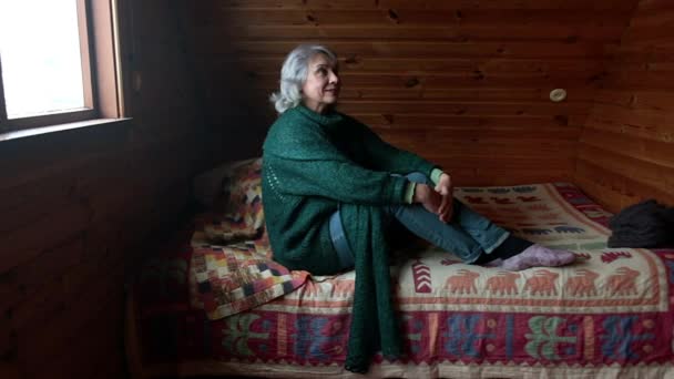 Mujer mayor se sienta en una habitación de madera y solo mira en diferentes direcciones. — Vídeo de stock
