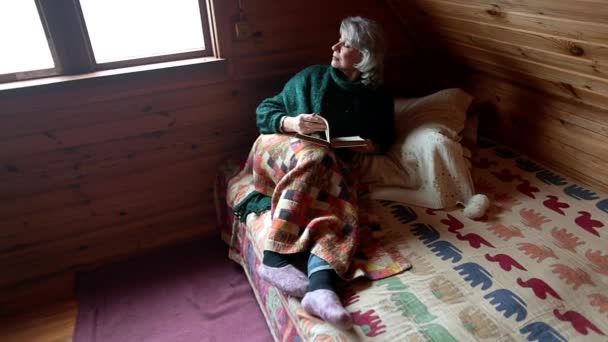 Kobieta w podeszłym wieku siedzi na łóżku pod kocem z książką w ręku — Wideo stockowe