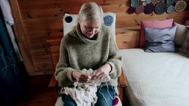 Взрослая женщина сидит на стуле и вяжет иголки. — стоковое видео