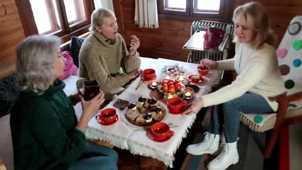 Τρεις ενήλικες γυναίκες κάθονται σε ένα τραπέζι μέσα στο σπίτι και πίνουν τσάι.. — Αρχείο Βίντεο
