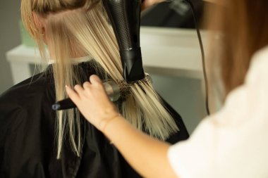 Saç kurutuculu eller ve taraklı saçlar sarışının saçlarını kurutur. Arkadan bak..