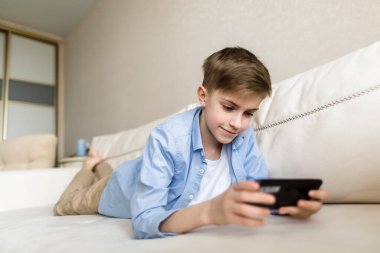 Çocuk elinde telefonla kanepede uzanıyor, onunla oynuyor..