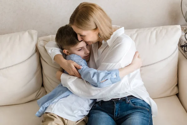 Dospělá žena sedí s teenagerem na gauči, klábosí a objímají. — Stock fotografie