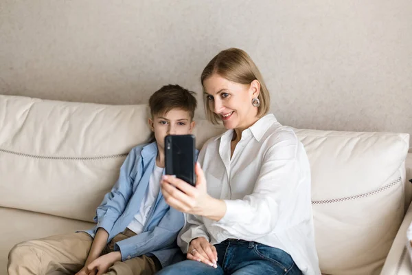 Chłopiec i dorosła kobieta robią sobie selfie przez telefon siedząc na kanapie. — Zdjęcie stockowe