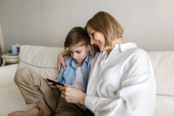 Yetişkin kadın ve çocuk kanepede oturup birlikte telefona bakıyorlar.