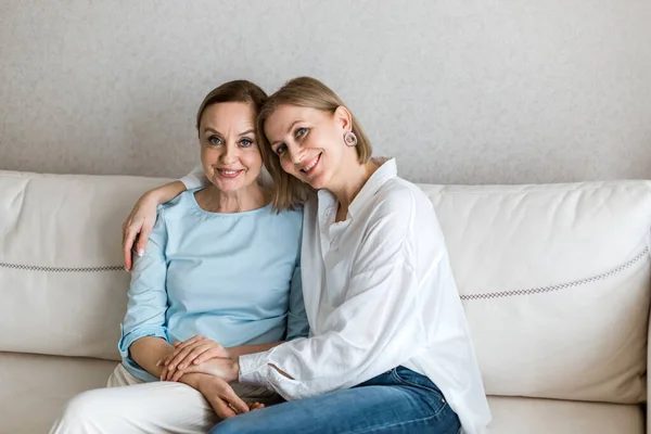 Dvě dospělé ženy sedí na gauči, objímají se a dívají se do kamery. — Stock fotografie