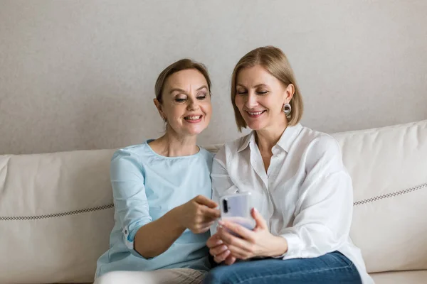 İki kadın kanepede oturuyor ve konuşurken telefona bakıyor..