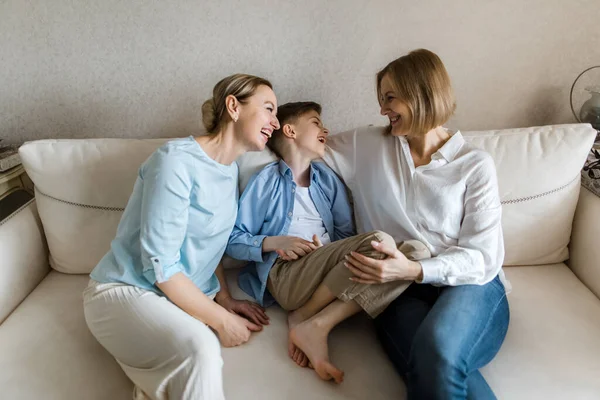 Két felnőtt nő és egy gyerek ül a kanapén, beszélgetnek és mosolyognak.. — Stock Fotó