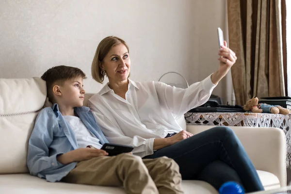 Fiú és felnőtt nő, csináljatok egy szelfit a telefonon, miközben a kanapén ülnek.. — Stock Fotó