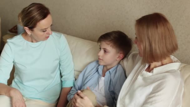 Due donne adulte e un bambino sono seduti sul divano, a chiacchierare e sorridere. — Video Stock