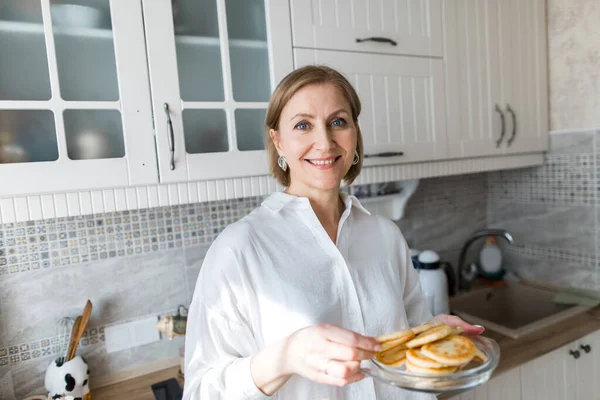 Yetişkin bir kadın mutfakta duruyor ve ellerinde krep tutuyor..