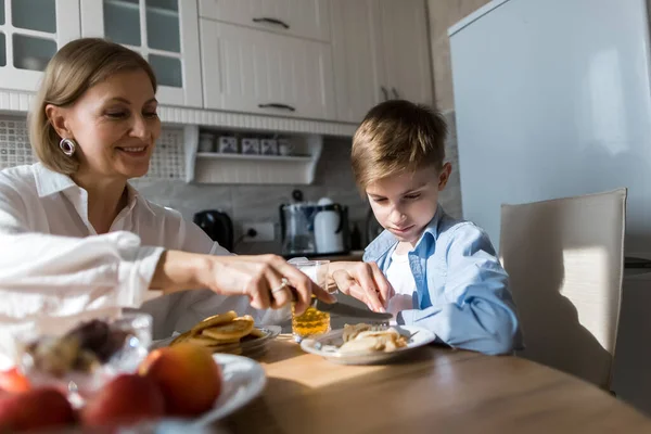 Adult woman in the kitchen treats a child with pancakes and juice. — Stock Photo, Image