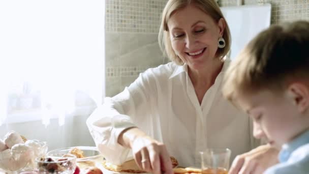 Vuxen kvinna i köket behandlar ett barn med pannkakor och juice. — Stockvideo