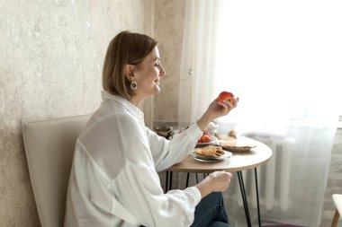 Kadın bir masada oturuyor, elinde bir elma, bir elmaya bakıyor..