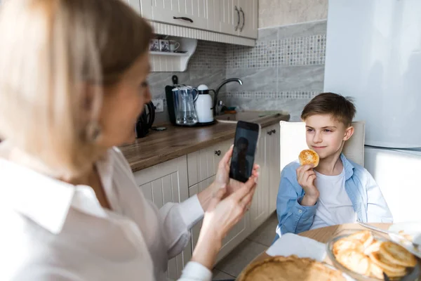 Mutfaktaki kadın çocuğun fotoğrafını çekiyor, kahvaltıyı masaya koyuyor..
