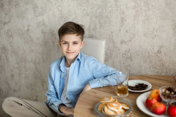 Çocuk mutfaktaki masaya oturur ve kameraya bakar..