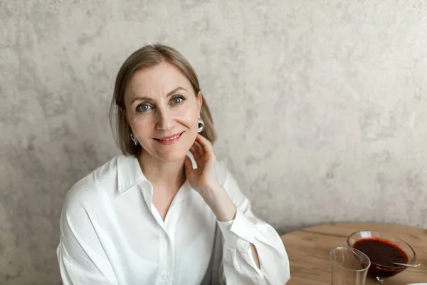 Kadın mutfakta oturuyor, gülümsüyor ve kameraya bakıyor. Portre.