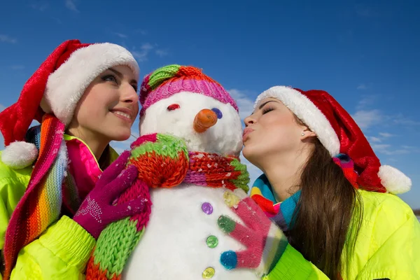 Dvě mladé ženy líbání sněhulák — Stock fotografie