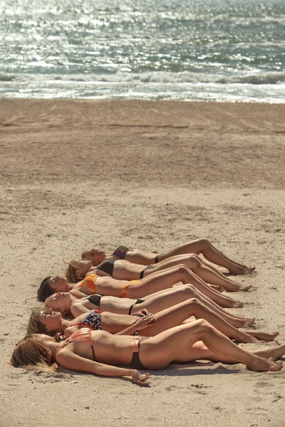 Verschillende meisjes in bikini, liggend op het zandstrand — Stockfoto