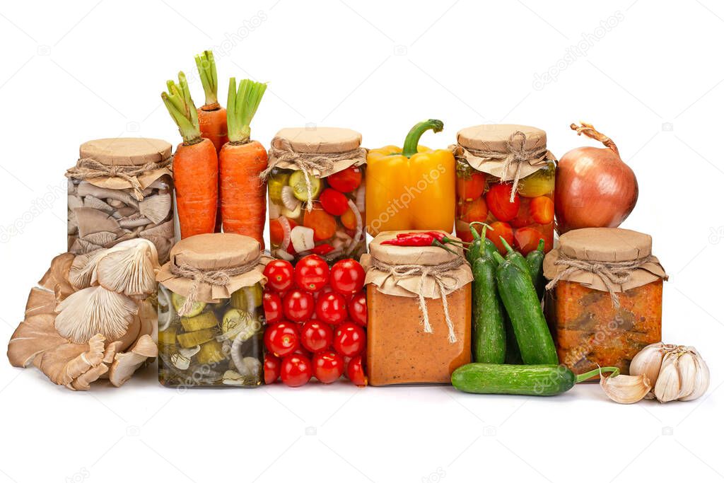 Preserved vegetables in glass jars with fresh vegetables isolated on white background