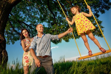 Girl on  swing with parents clipart