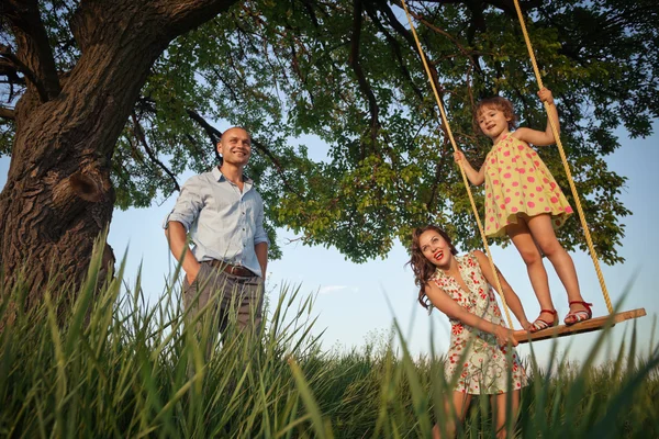 Meisje op schommel met ouders — Stockfoto