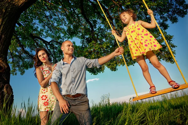 Meisje op schommel met ouders — Stockfoto