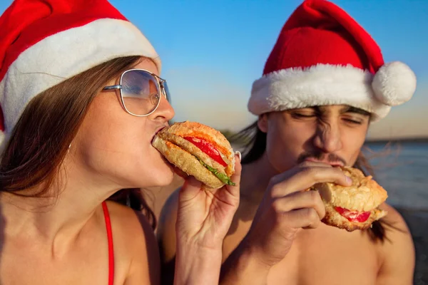 Para w Santa kapelusze jedzenie fast food — Zdjęcie stockowe