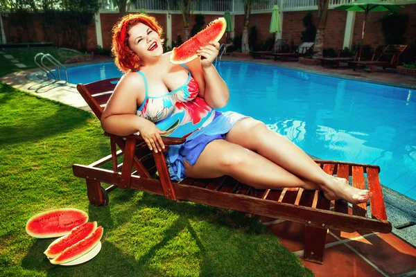 Donna in sovrappeso mangiare anguria a bordo piscina Foto Stock Royalty Free
