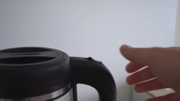 Seething water with bubbles boils in transparent glass electric kettle. Man boiling water in an electric kettle on white background. 4k stock footage. — Stock Video