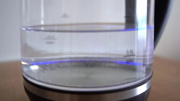 泡のある水は透明なガラス電気ケトルに沸騰します。白い背景に電気ケトルで水を沸かす男。4kストック映像. — ストック動画