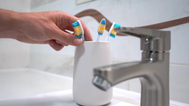 Photo d'adultes main qui prend une brosse à dents de verre en plastique qui se tient près du lavabo. Images du stock 4k. — Video