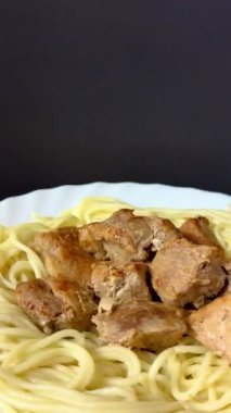 Close-up shot of spaghetti with fried pork pieces on a white plate. Cooking delicious food at home.