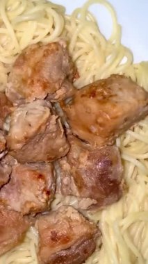 Close-up shot of spaghetti with fried pork pieces on a white plate. Cooking delicious food at home.