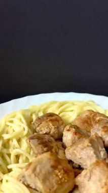 Close-up shot of spaghetti with fried pork pieces on a white plate. Cooking delicious food at home.