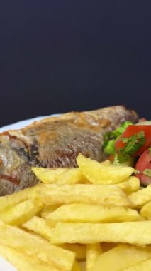A close-up shot of fried potatoes, fried fish, and a salad with fresh vegetables and herbs. Cooking delicious food at home.