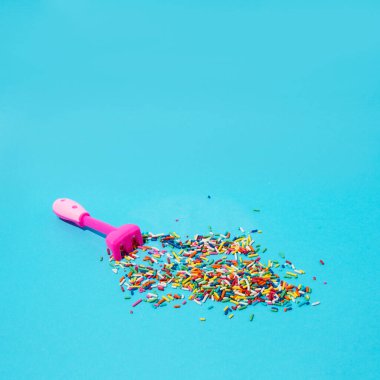 Pembe bahçe tırmığı ve küçük renkli şekerler. Yumuşak mavi bir arkaplanda.