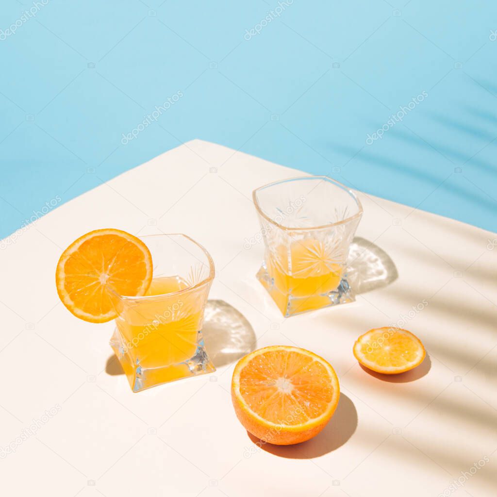 Summer tropical composition with yellow orange juices in a glass on the table with the shade of a palm leaf.