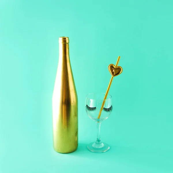 A glass and a gold bottle with eyelashes and a gold tube with a heart. Celebration. Turquoise background.