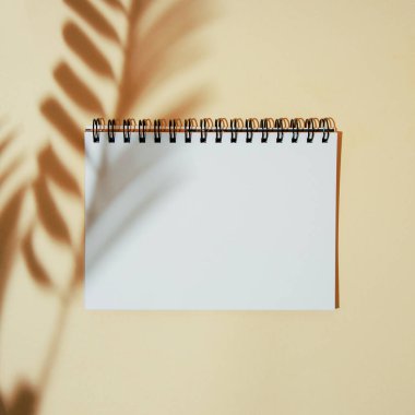 Palmiye yapraklarının gölgesi beyaz bir defter kağıdının üzerinde. Metin için yeri var. Sarı arkaplandaki yaprak siluetleri.