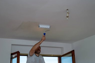 Çalışkan adam tavanı beyazla boyuyor.