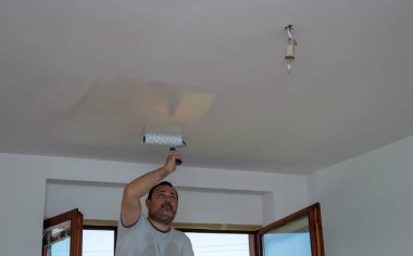 Çalışkan adam tavanı beyazla boyuyor.