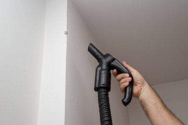 Elektrikli süpürge tutan bir adamın eli. Duvardaki kiri temizlerken.