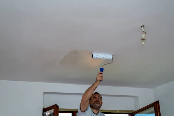 Hard working man painting ceiling with a roller in white