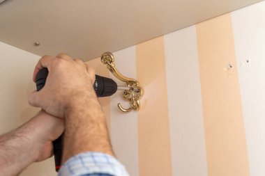 Adam dekoratif gardırop kancası takarken tornavida kullanıyor.